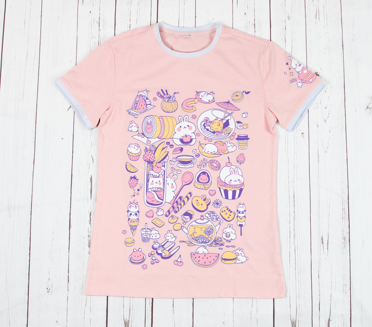 Light peach pink bunny t-shirt showing sweet bunny chefs making baking and café goods such as sweets, drinks, and desserts. The left sleeve of the shirt also shows a bunny sitting on a pink macraon. Light-weight and stretchable material that is made of 100% cotton. The collar and sleeve ends have cute white borders that truly frames the look of this summer shirt. Available in sizes XXS to 2XL.  