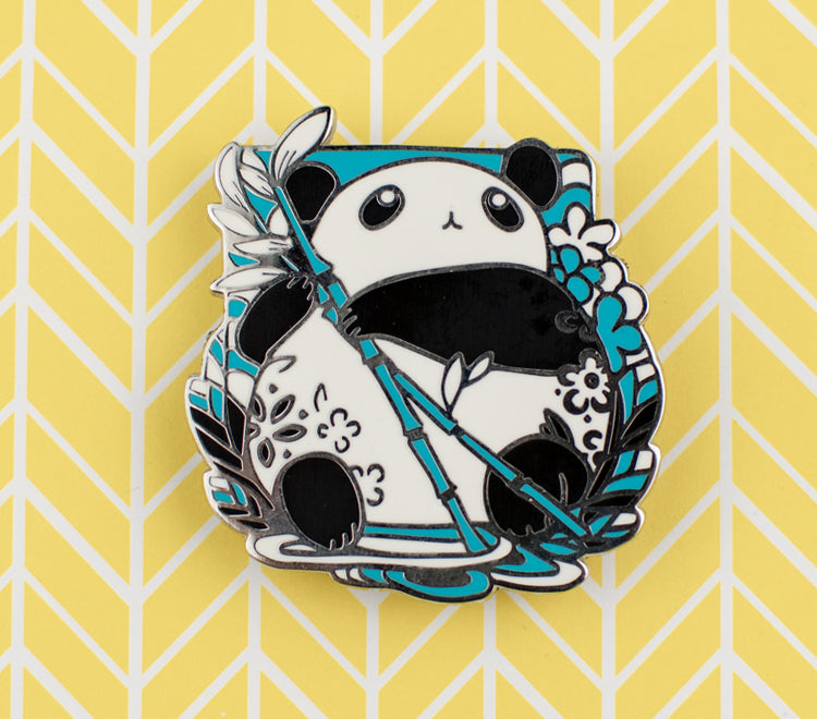 The pin design features a chibi panda holding a bamboo stem and looking up. The pin is printed on silver metal and has two rubber back pins in place for you to attach the pin to your clothes, bags, etc.  